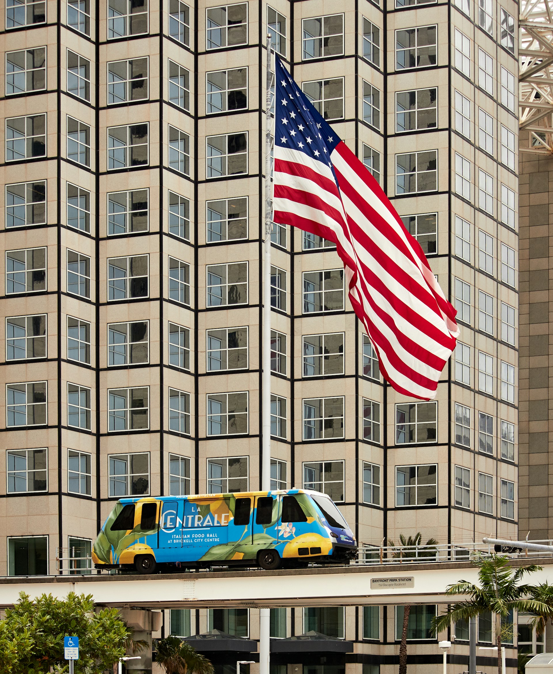 Miami Metromover passing downtown high-rises beneath an American flag