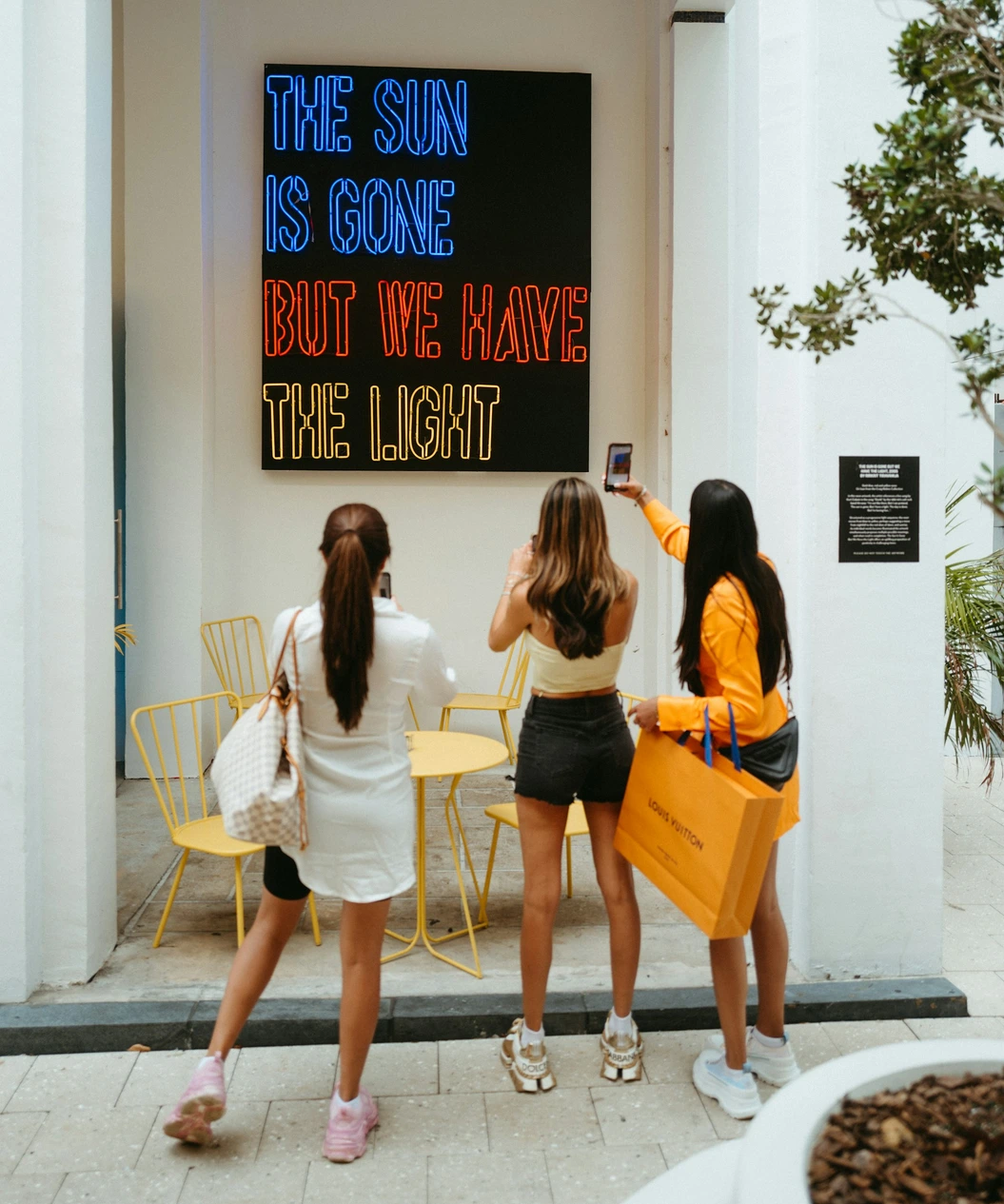 Three people photographing an illuminated sign on a storefront